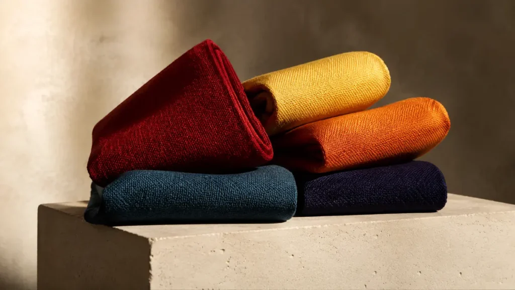 Five folded textiles in blue, red, yellow, orange and indigo balance on an ivory pedestal.