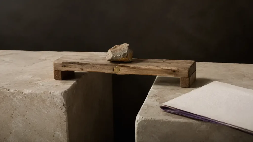 A rough wooden prototype bridge carries a stone across a gap, held by one brass pin.