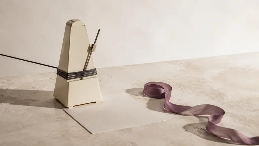 An ivory metronome bound by cord sits beside a blank card and a freely unwinding purple ribbon.